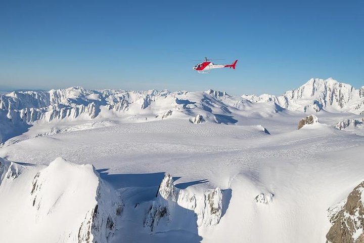 Helikopter auf dem Schnee über dem Fox Glacier mit Westküstentälern darunter